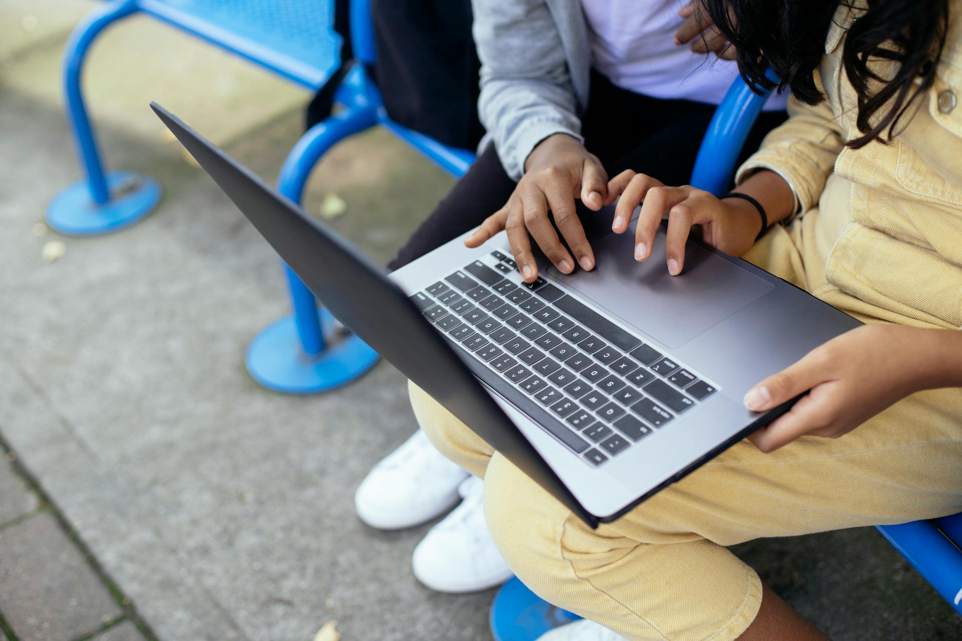 High angle of crop anonymous diverse schoolkids surfing internet on portable computer on urban bench