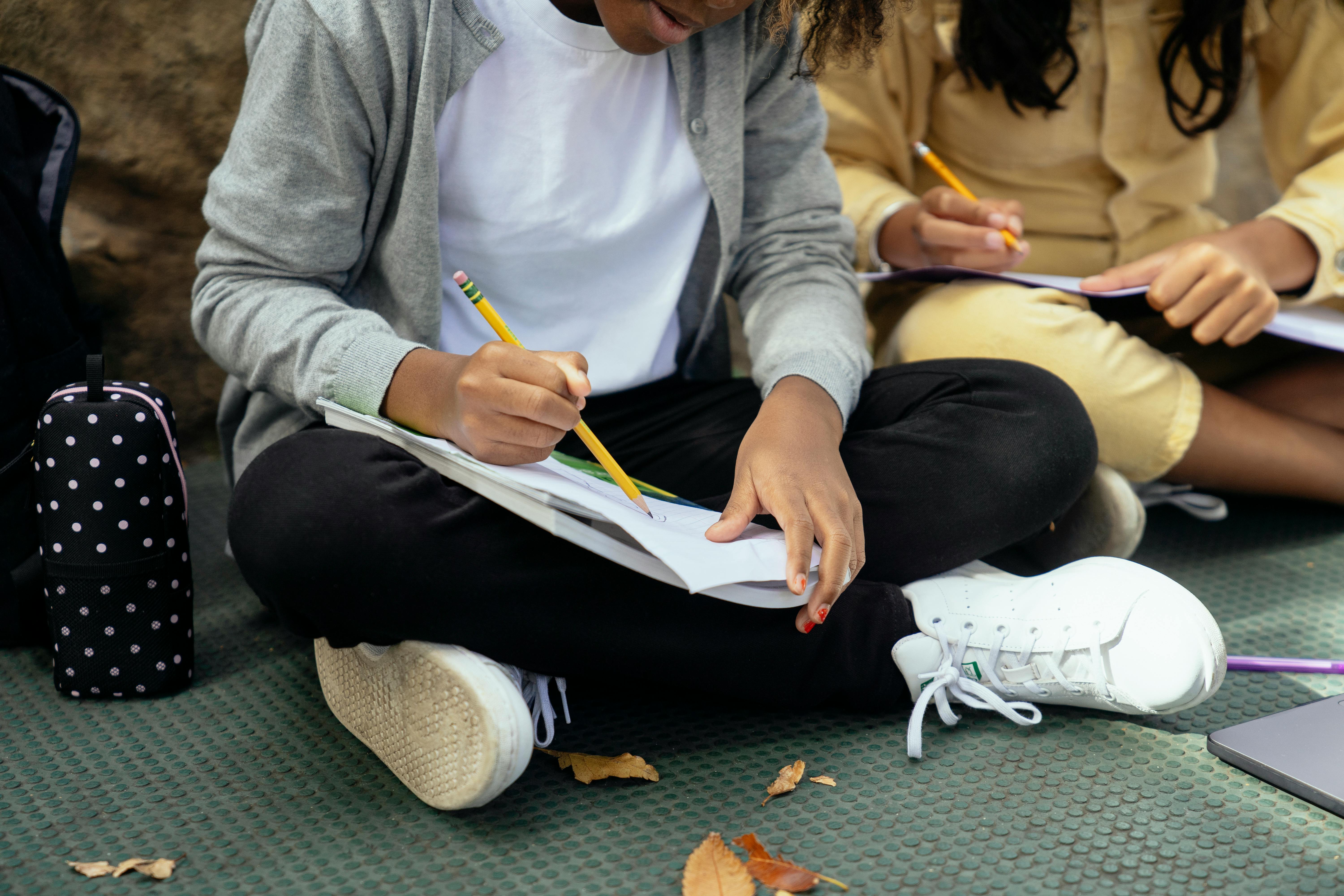 crop diverse schoolchildren doing homework on urban pavement