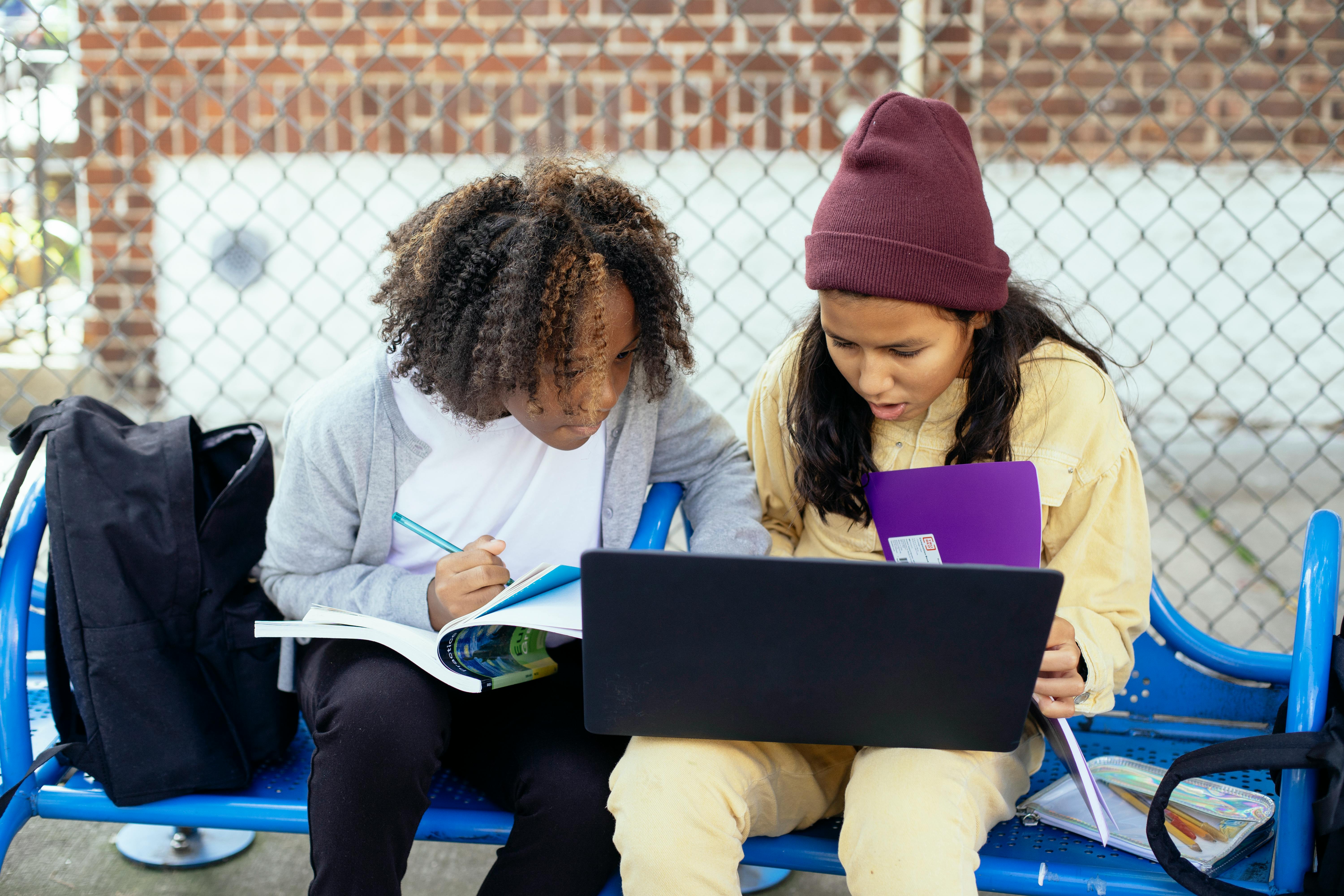 attentive multiracial schoolchildren with laptop doing homework on street bench