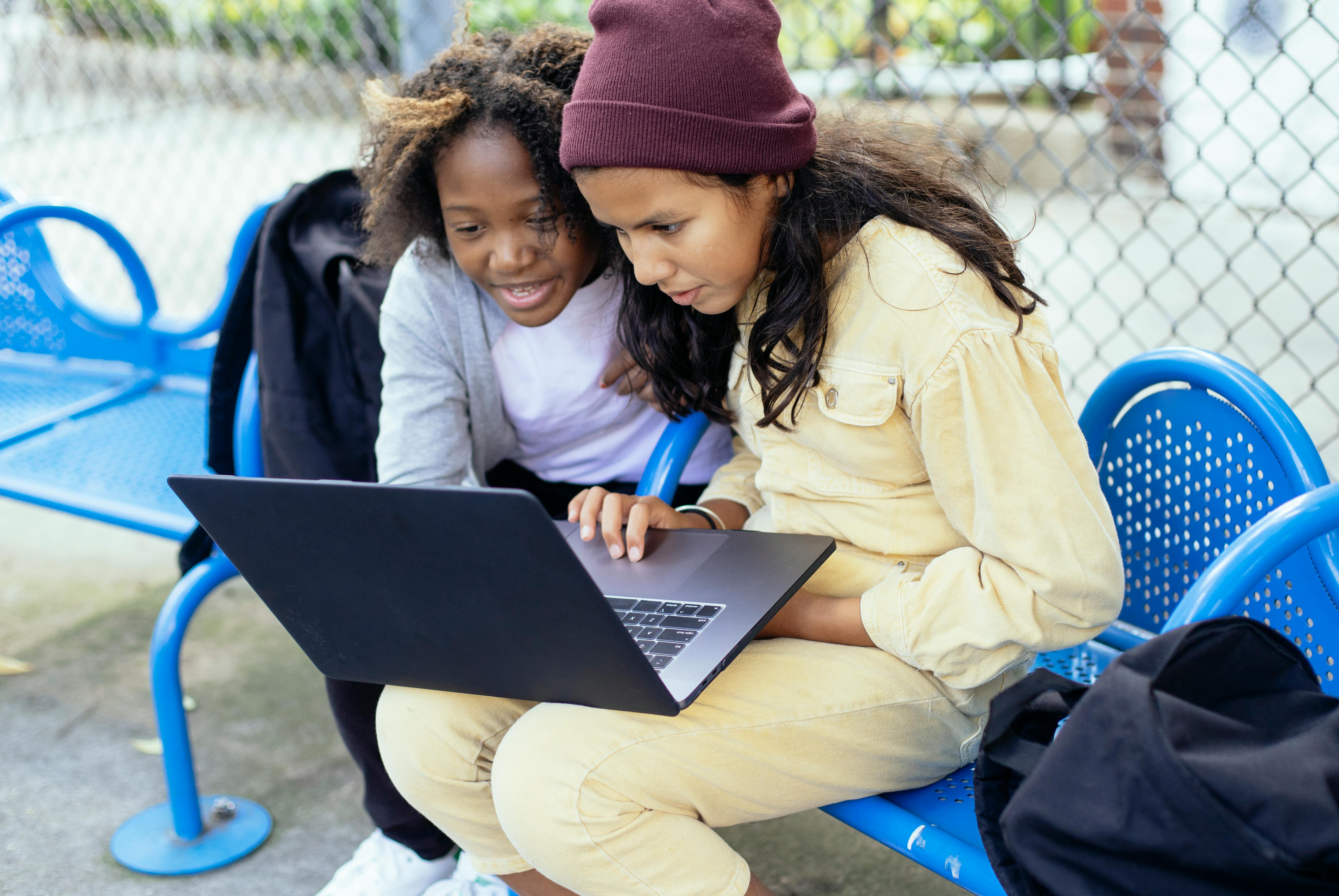 crop multiethnic schoolchildren watching laptop on urban bench