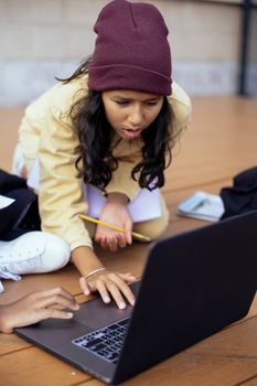 一个专注的女孩戴着无檐帽，坐在户外用笔记本电脑做作业