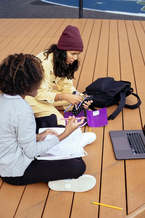 From above side view of anonymous focused multiracial schoolchildren watching netbook while sitting with copybooks and doing homework on street