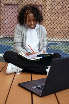 细心的民族学童盘腿坐在上网本附近，一边做作业一边在纸上记笔记