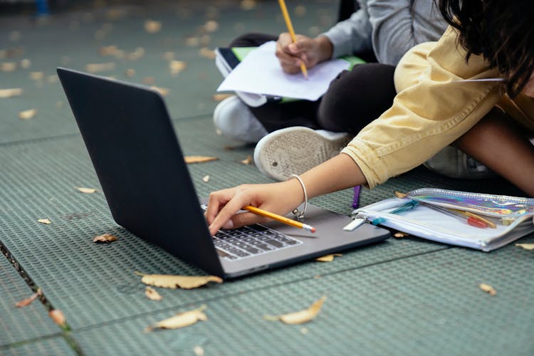 Faceless Diverse Schoolchildren Typing On Laptop While Studying On Street