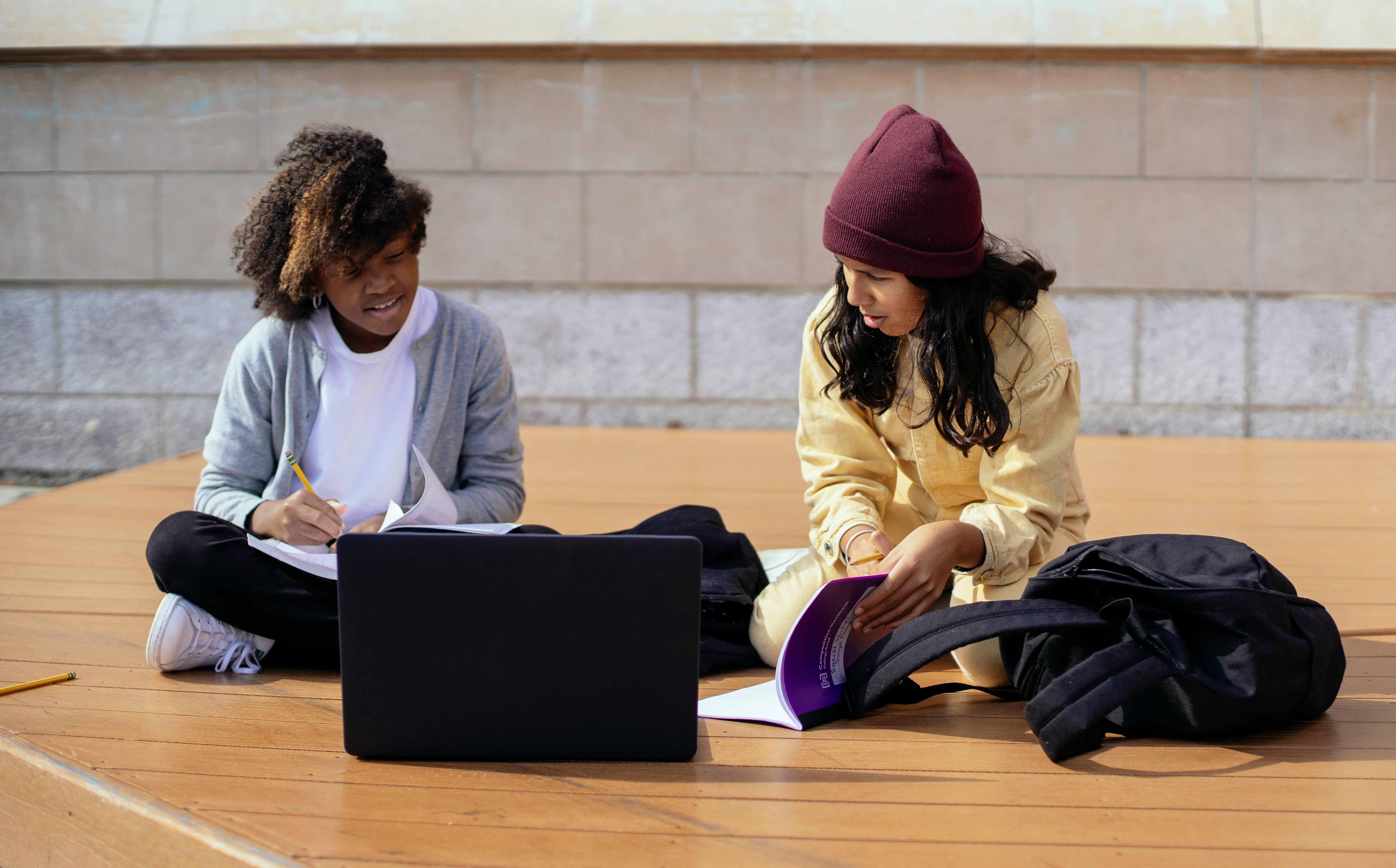 diverse schoolgirls talking while studying near laptop on street