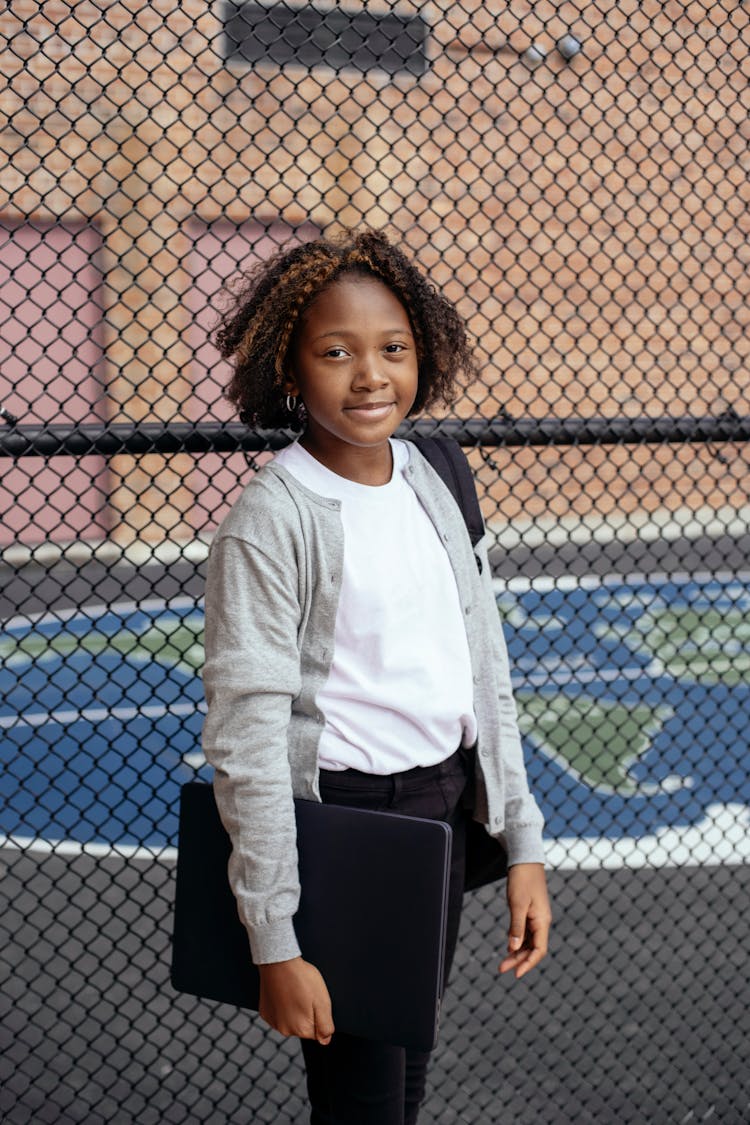 Cheerful Black Girl With Laptop In Schoolyard