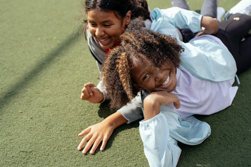 Cheerful multiracial girls lying on sports ground and smiling while spending sunny day together