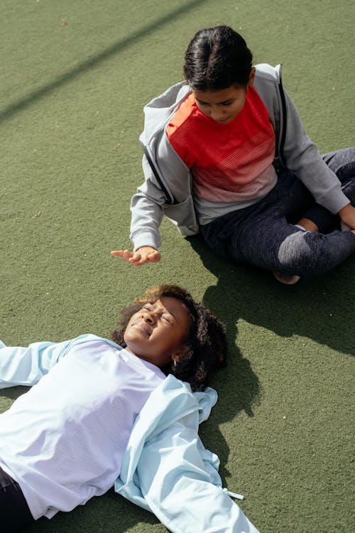 From above of multiracial schoolgirls having fun while resting after training on stadium in sunny weather