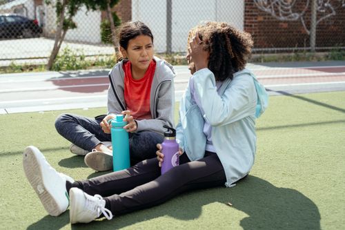 Free Full body of serious girls in sportswear holding bottles of water and resting on stadium while looking at each other Stock Photo
