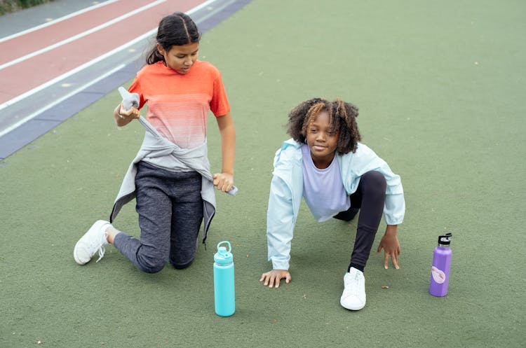 Smiling Black Girl Stretching Before Training With Friend On Running Track