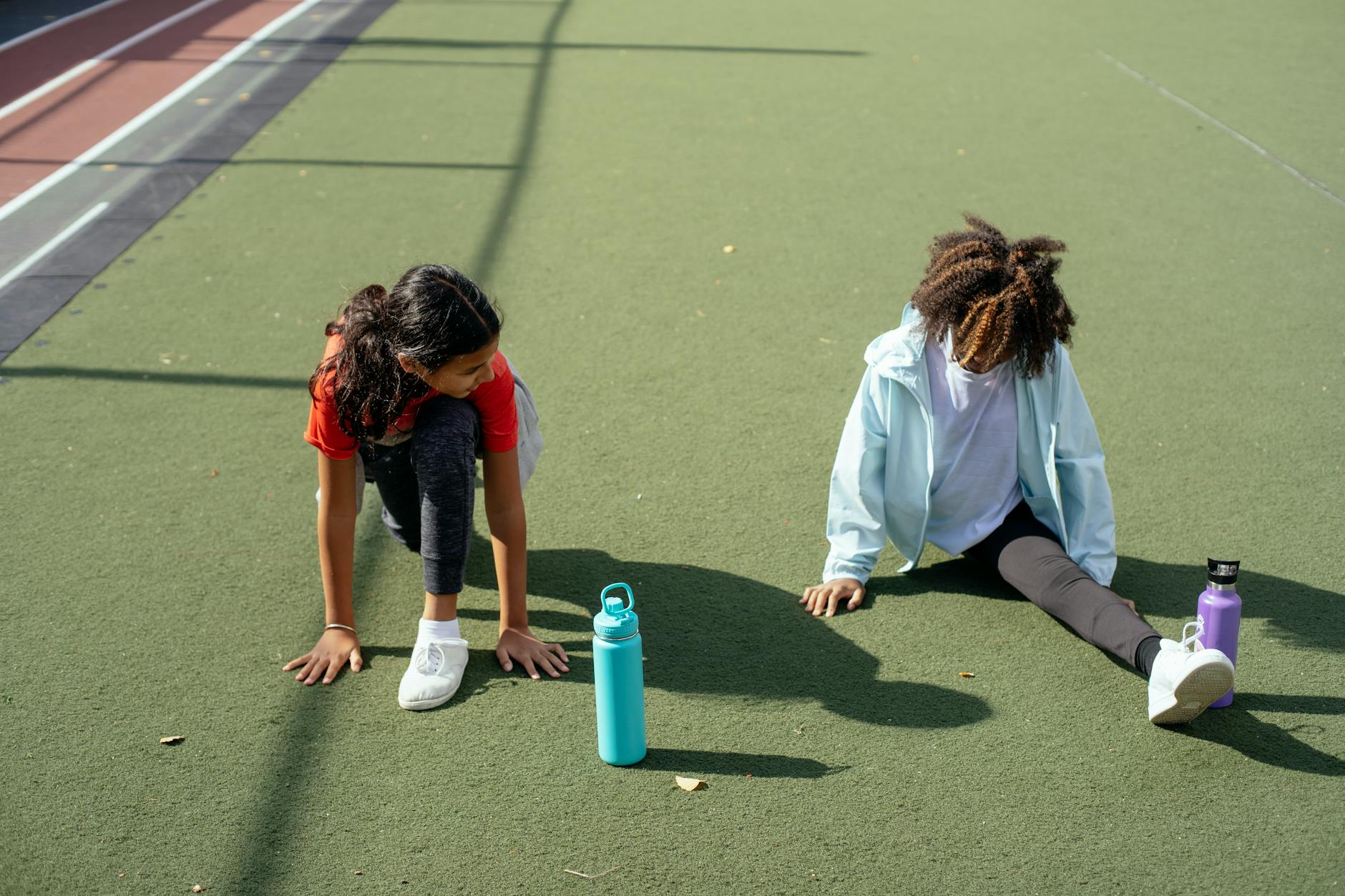 Black girl doing split while friend stretching before training on stadium