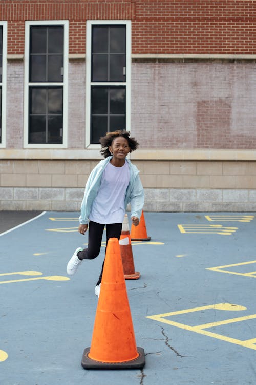 Happy black girl running around red cones on playground near school