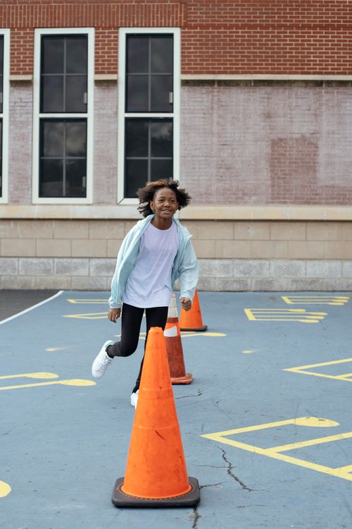 Free Happy African American kid wearing sportive outfit running around red cones located on backyard of school while resting after lessons Stock Photo