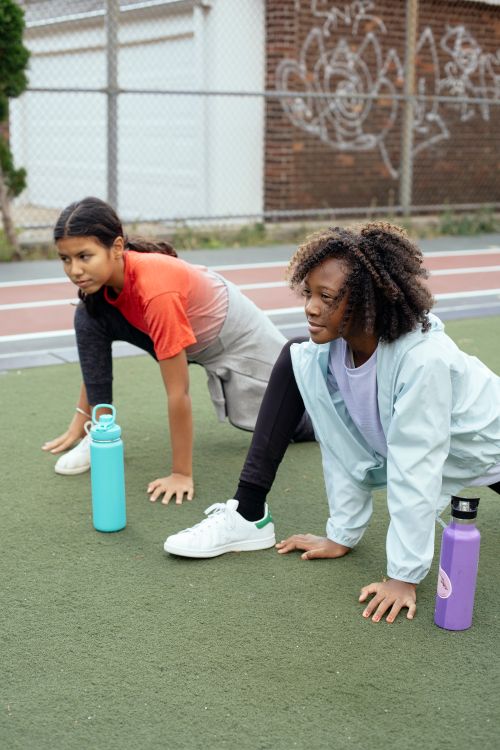 Free Concentrated diverse schoolgirls in sportswear warming up on sports ground during physical education class Stock Photo