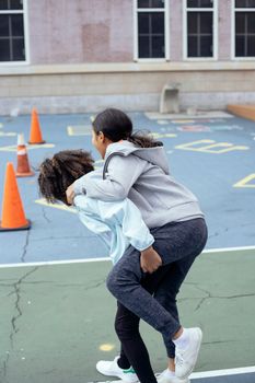Back view of unrecognizable multiracial girls in sportswear doing piggyback riding during physical education class