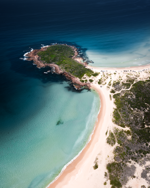 A breathtaking aerial view of Boomerang Beach, showcasing crystal clear waters and lush greenery.