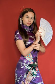 一位穿着传统丝绸连衣裙的妇女，手持一把红色背景的装饰扇子