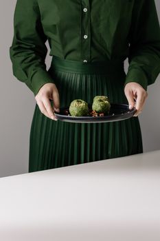 一位身着优雅绿色服装的女性，双手在黑色盘子上展示素食格鲁吉亚菠菜普卡利
