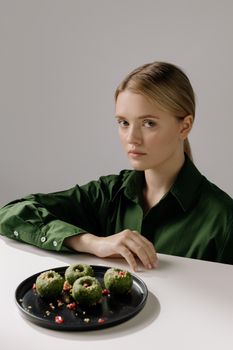 A woman in a green shirt poses with a plate of traditional Georgian spinach pkhali, reflecting vegan cuisine.