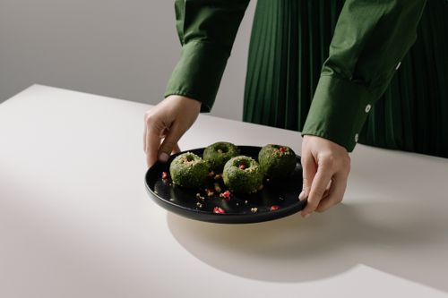 Free Hands presenting a black plate with spinach pkhali, showcasing traditional Georgian vegan cuisine. Stock Photo