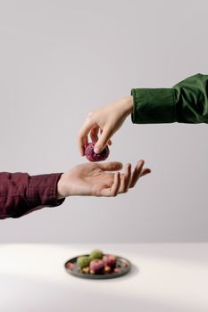 Close-up of two hands exchanging Georgian beetroot pkhali on a minimalist grey background.