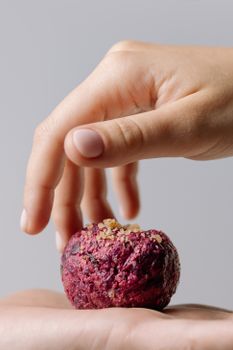 A hand delicately holds a vibrant beetroot pkhali, showcasing Georgian vegetarian cuisine.