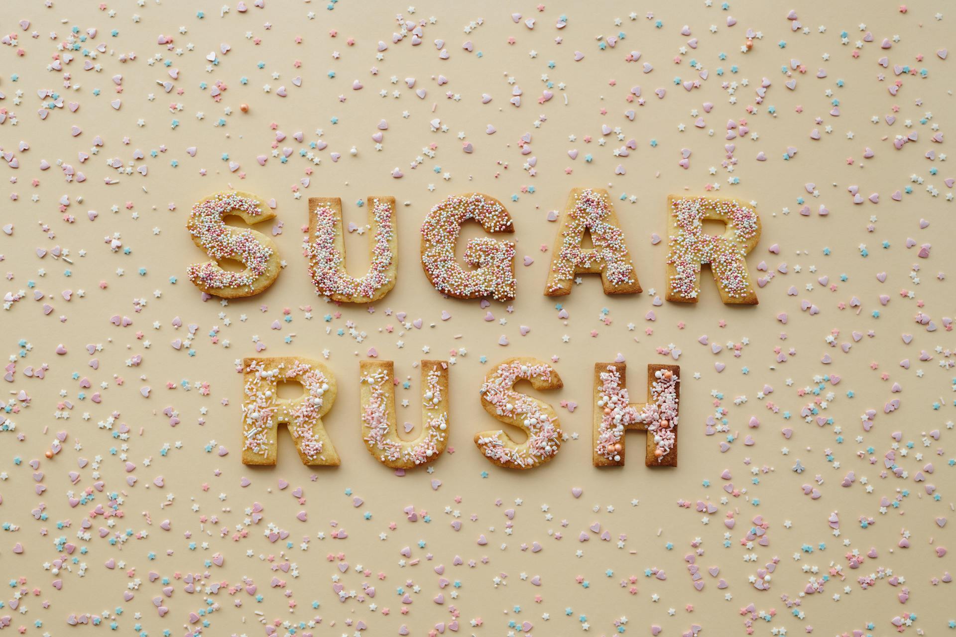 Top view of alphabet-shaped sugar cookies with colorful sprinkles spelling 'SUGAR RUSH'.