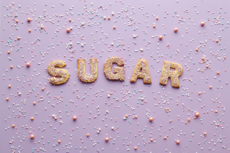 Colorful sprinkle-covered cookies spelling 'sugar' on a pastel purple background, creating a sweet and playful flatlay design.