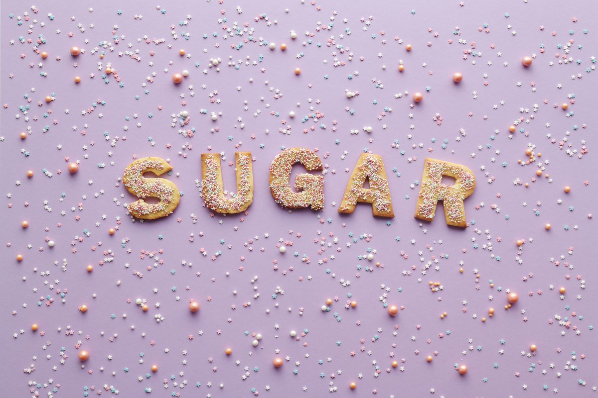 Colorful sprinkle-covered cookies spelling 'sugar' on a pastel purple background, creating a sweet and playful flatlay design.