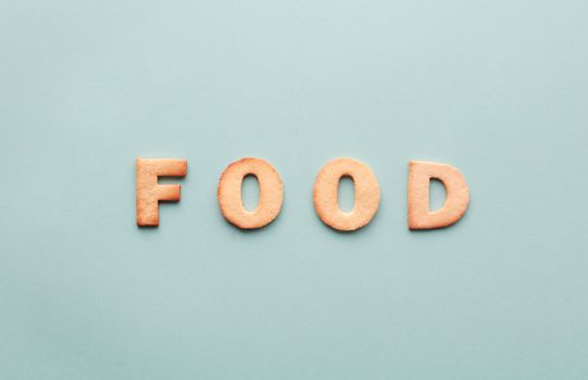 Flat lay of alphabet cookies spelling 'FOOD' on a turquoise background.