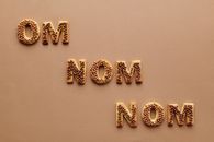 Sweet letter-shaped cookies spelling 'OM NOM NOM' on a brown surface.