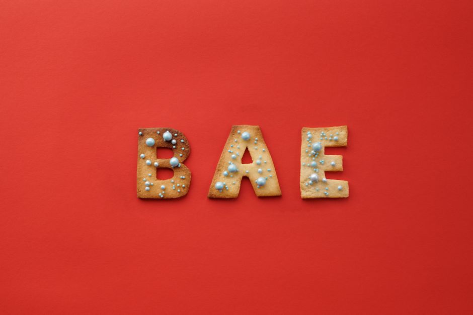 Letter-shaped cookies spelling 'BAE' adorned with sprinkles on a vibrant red background.
