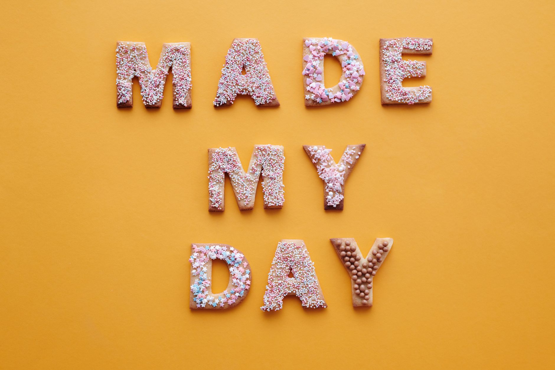 Colorful alphabet cookies spelling 'Made My Day' on a vibrant yellow background.