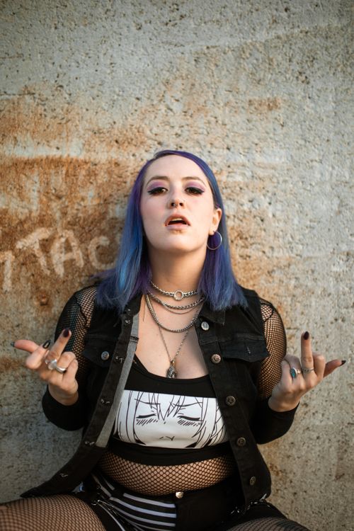 Free Portrait of a young woman with purple hair in edgy street fashion posing against a concrete wall. Stock Photo