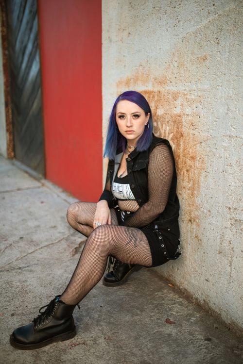 Free A trendy young woman with purple hair poses against a concrete wall, showcasing her unique street style. Stock Photo