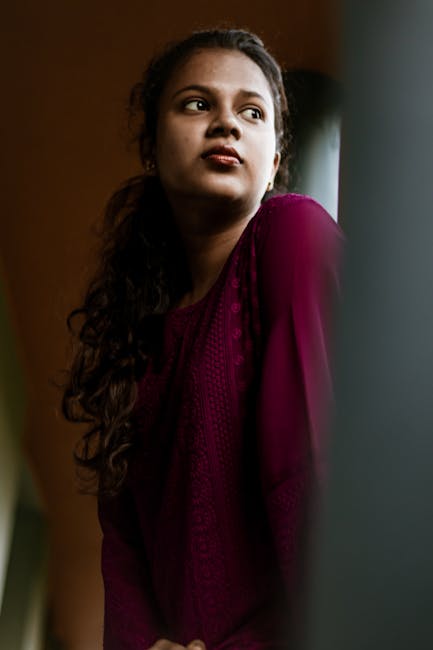 Portrait of a young woman with curly hair in a maroon dress, looking thoughtfully away.