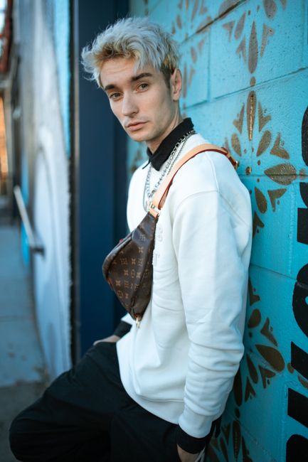 Portrait of a young man with trendy dyed hair and fashionable sling bag against an urban graffiti backdrop.