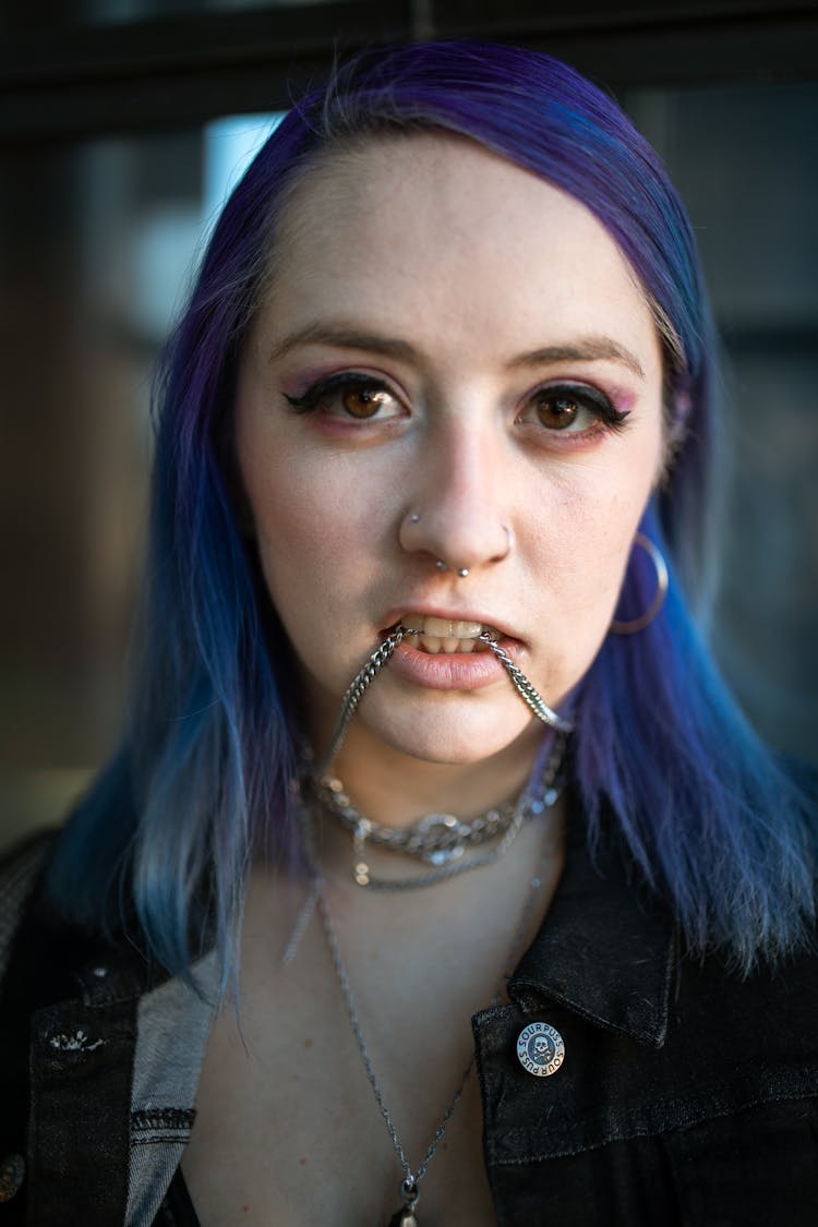 Woman With Purple Hair Biting Her Necklace While Looking At The Camera