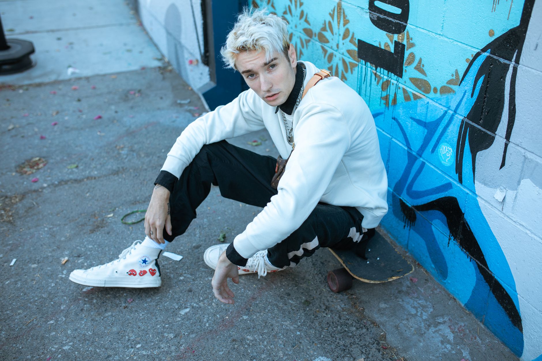 Portrait of a young man with dyed hair posing with a skateboard in an urban environment, showcasing street style.