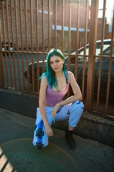 Stylish young woman with blue hair in edgy streetwear posing outdoors.