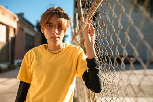 Person in Yellow Long Sleeve Shirt Standing Beside Gray Metal Fence while Looking at Camera