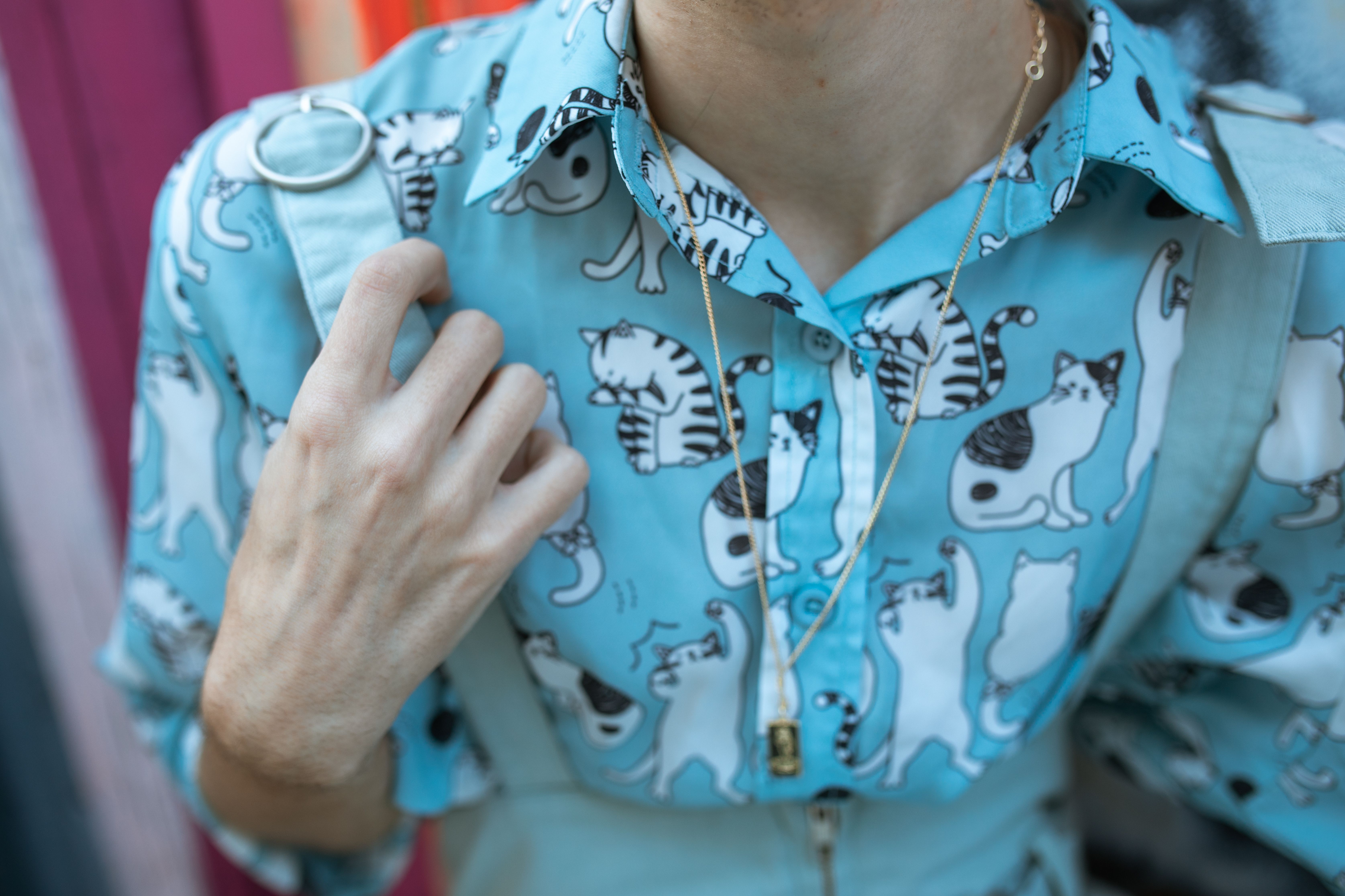 Close-up of a person wearing a trendy cat print shirt and a gold necklace, perfect for cat lovers.