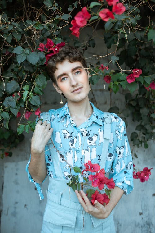 Person in Blue Button Up Shirt Standing Under Red Flowers