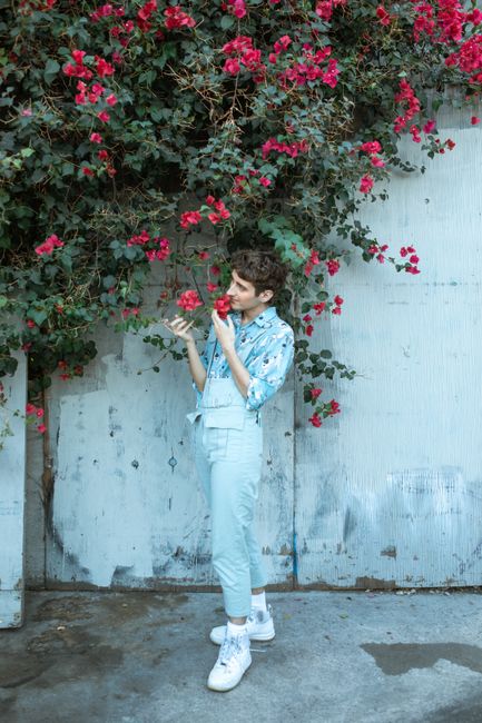 A young adult enjoying the scent of vivid red bougainvillea flowers against a textured wall.