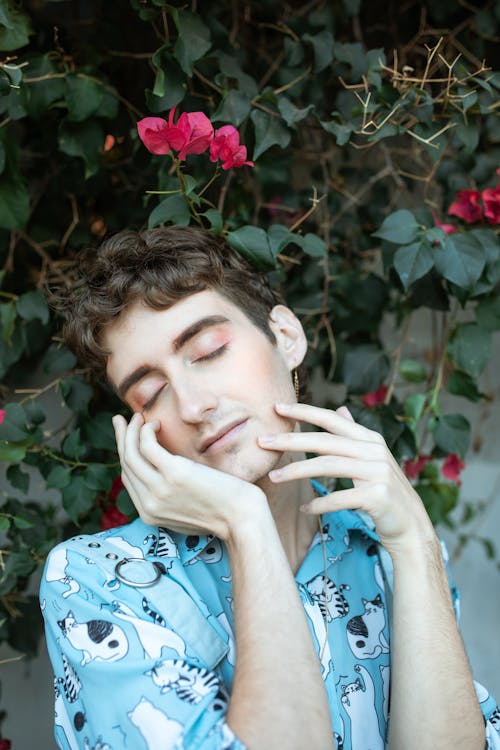 Person in Blue Button Up Shirt Standing Under Red Flowers with Closed Eyes