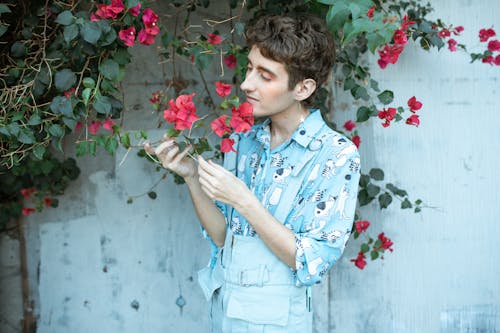 Person in Blue Button Up Shirt Standing Under Red Flowers
