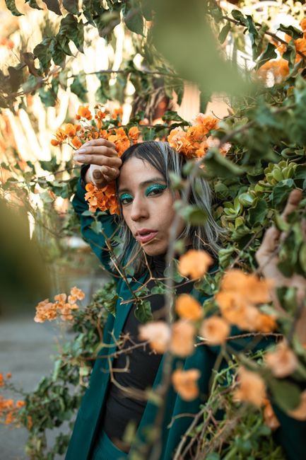 Fotomural Modelo posa con un maquillaje vívido entre exuberantes verdes y brillantes flores naranjas. Escena de moda urbana.