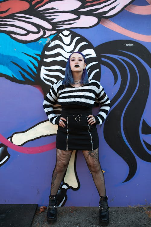 Woman in Black and White Striped Long Sleeve Shirt and Black Skirt Standing Beside Painted Wall 