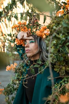 A striking portrait of a person surrounded by vivid orange flowers outdoors in fall.