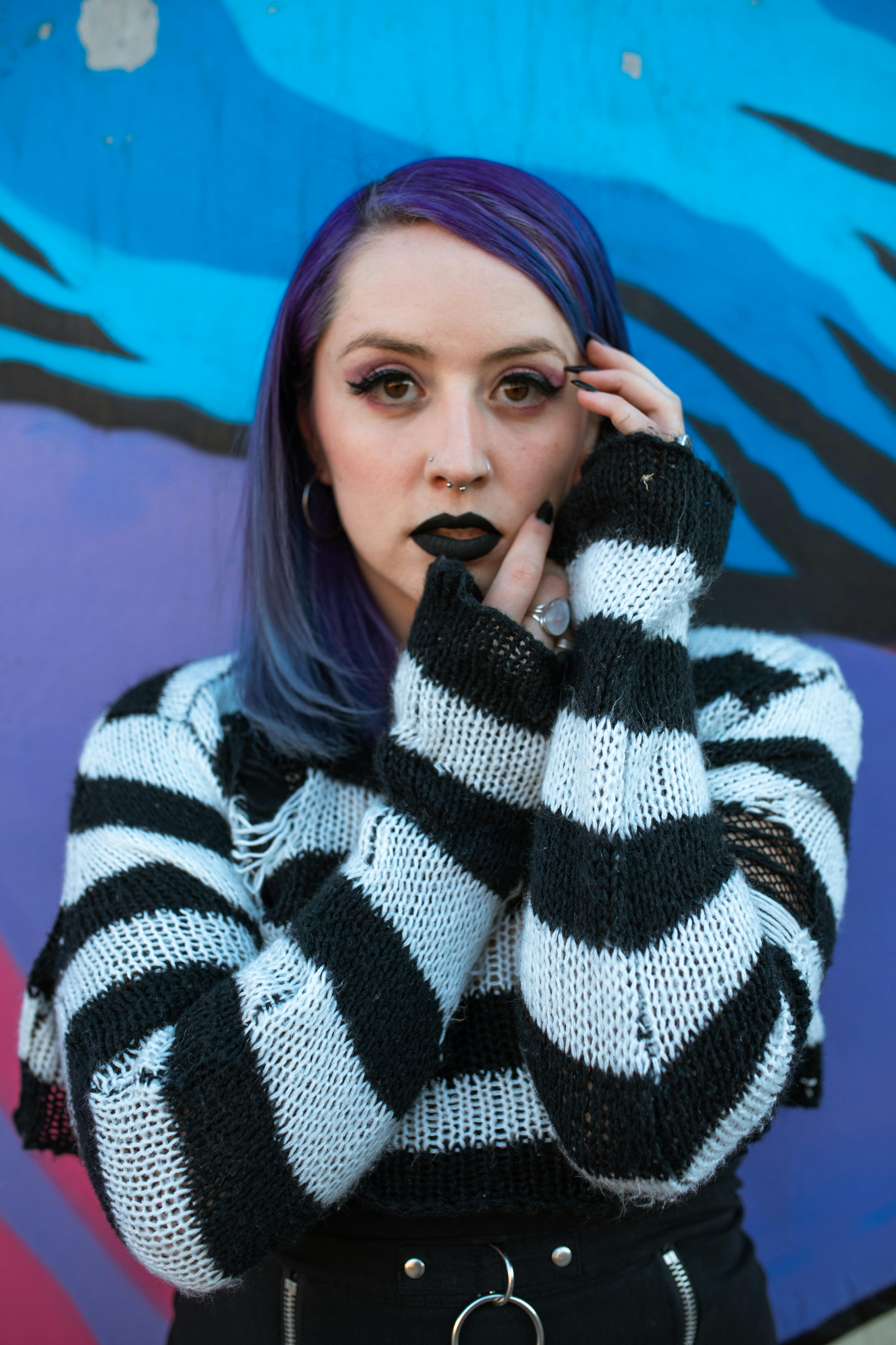 Stylish individual with purple hair and black lipstick against a colorful graffiti wall.
